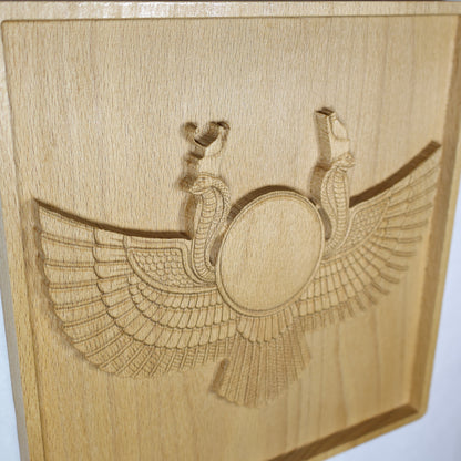 High side-angle view of an Egyptian Winged Sun Disk wood relief showing the raised sun emblem, cobra guardians, sweeping carved wings, recessed frame, and natural beech wood finish.
