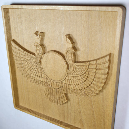 Left display-angle view of an Egyptian Winged Sun Disk wood relief with a raised sun circle, twin cobra guardians, broad carved wings, and natural beech wood finish.