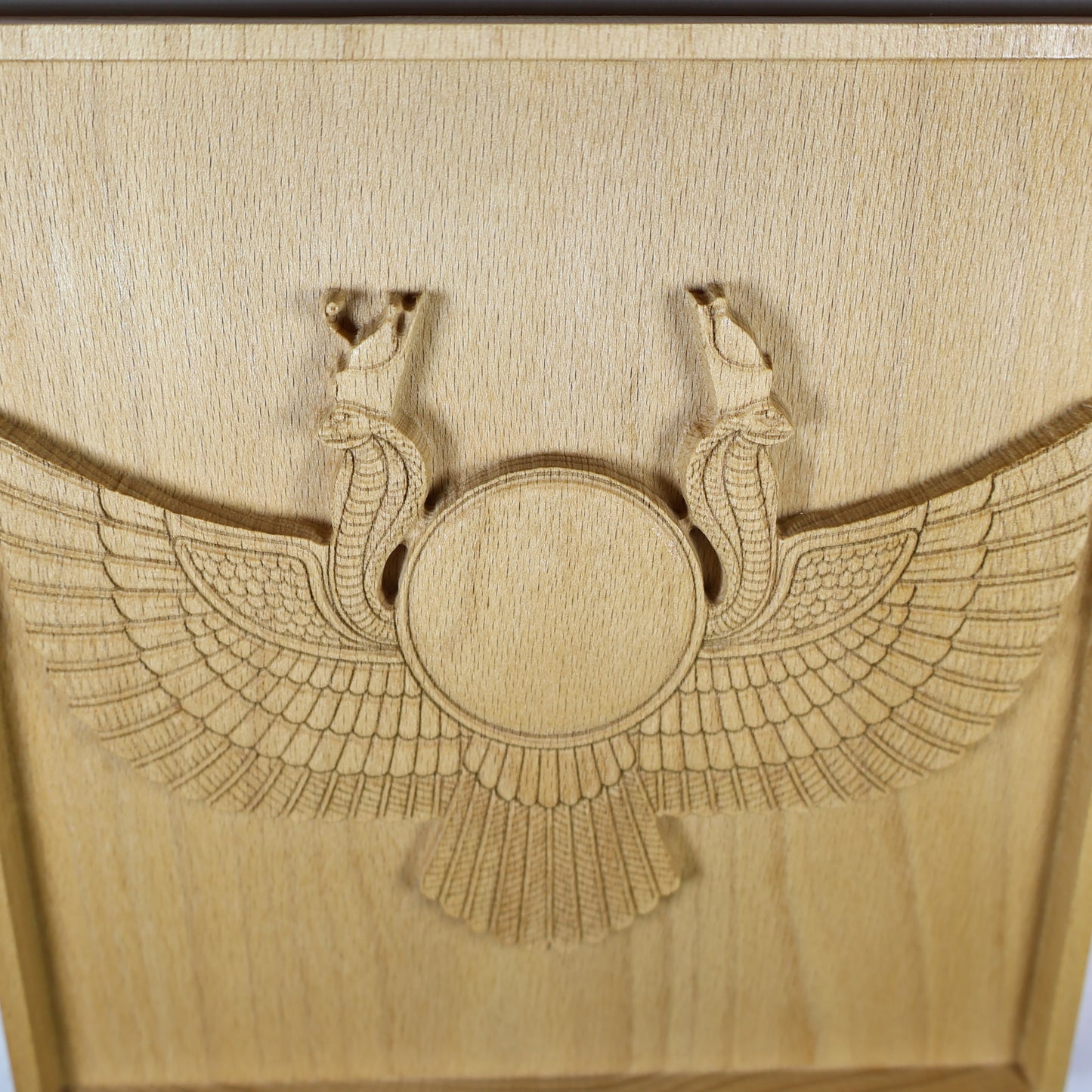 Close vertical view of an Egyptian Winged Sun Disk wood relief showing the sun disk, paired cobra details, sweeping feather wings, and natural beech wood finish.