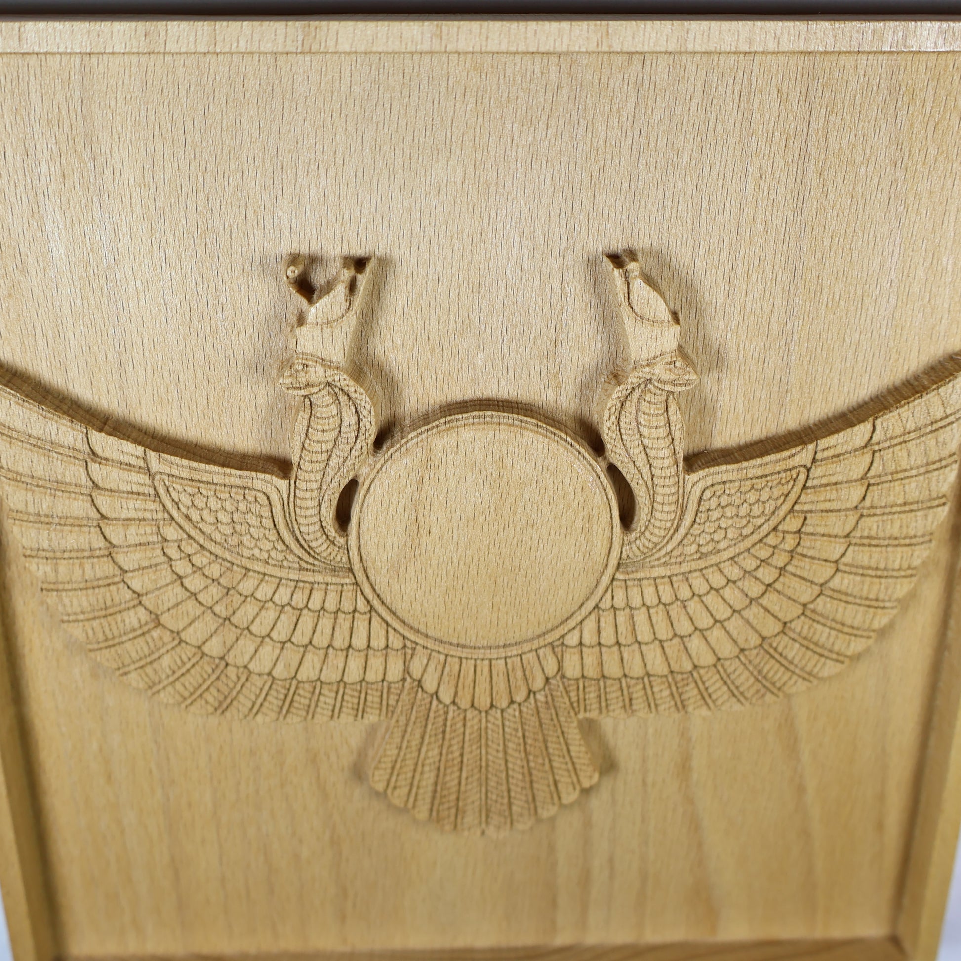 Close vertical view of an Egyptian Winged Sun Disk wood relief showing the sun disk, paired cobra details, sweeping feather wings, and natural beech wood finish.