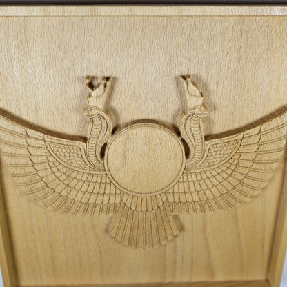 Close vertical view of an Egyptian Winged Sun Disk wood relief showing the sun disk, paired cobra details, sweeping feather wings, and natural beech wood finish.