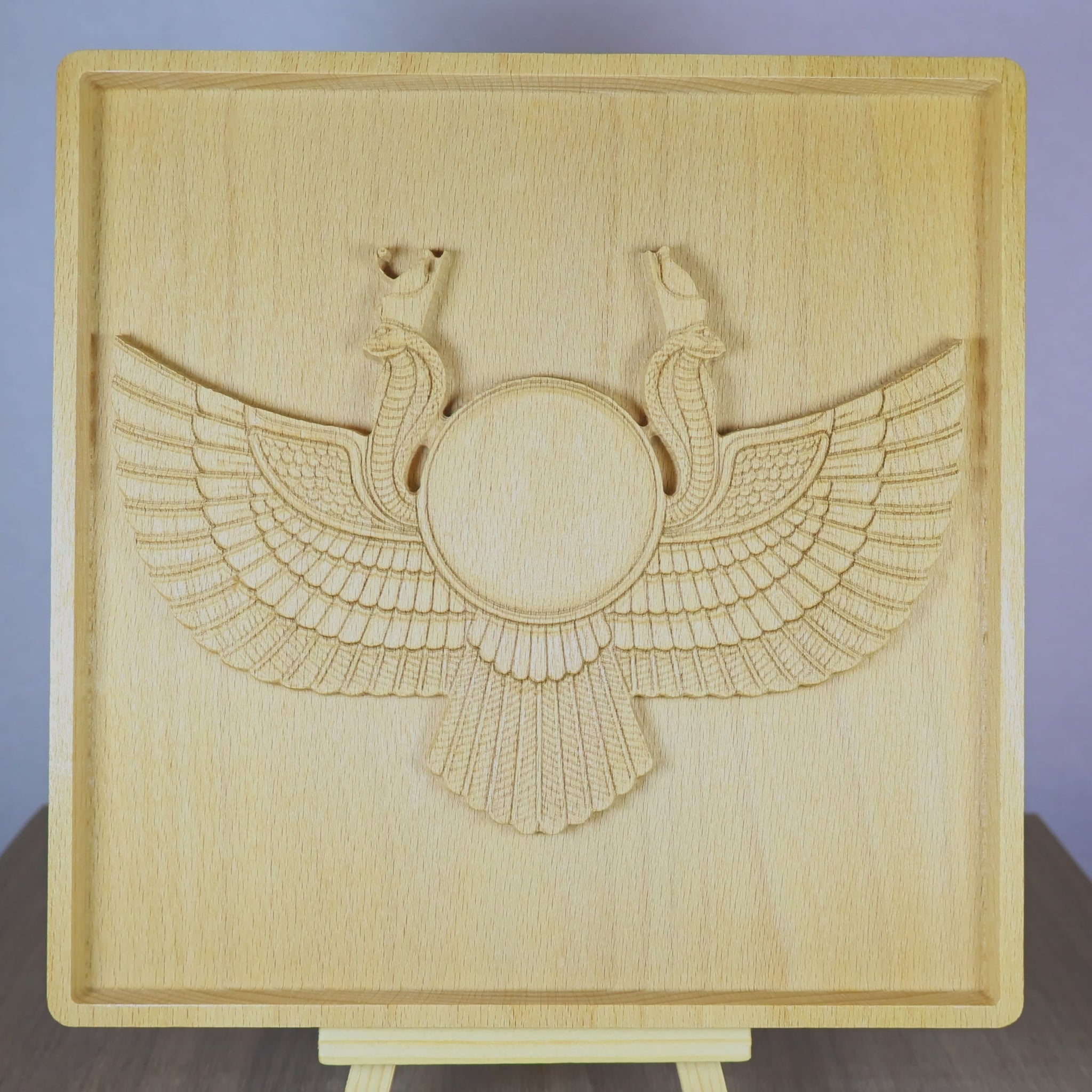 Rotating tabletop video of an Egyptian Winged Sun Disk wood relief, showing the front and angled side views of the carved Ra-Horus sun symbol, wide feathered wings, twin uraeus cobras, raised bas relief depth, and natural beech wood finish.