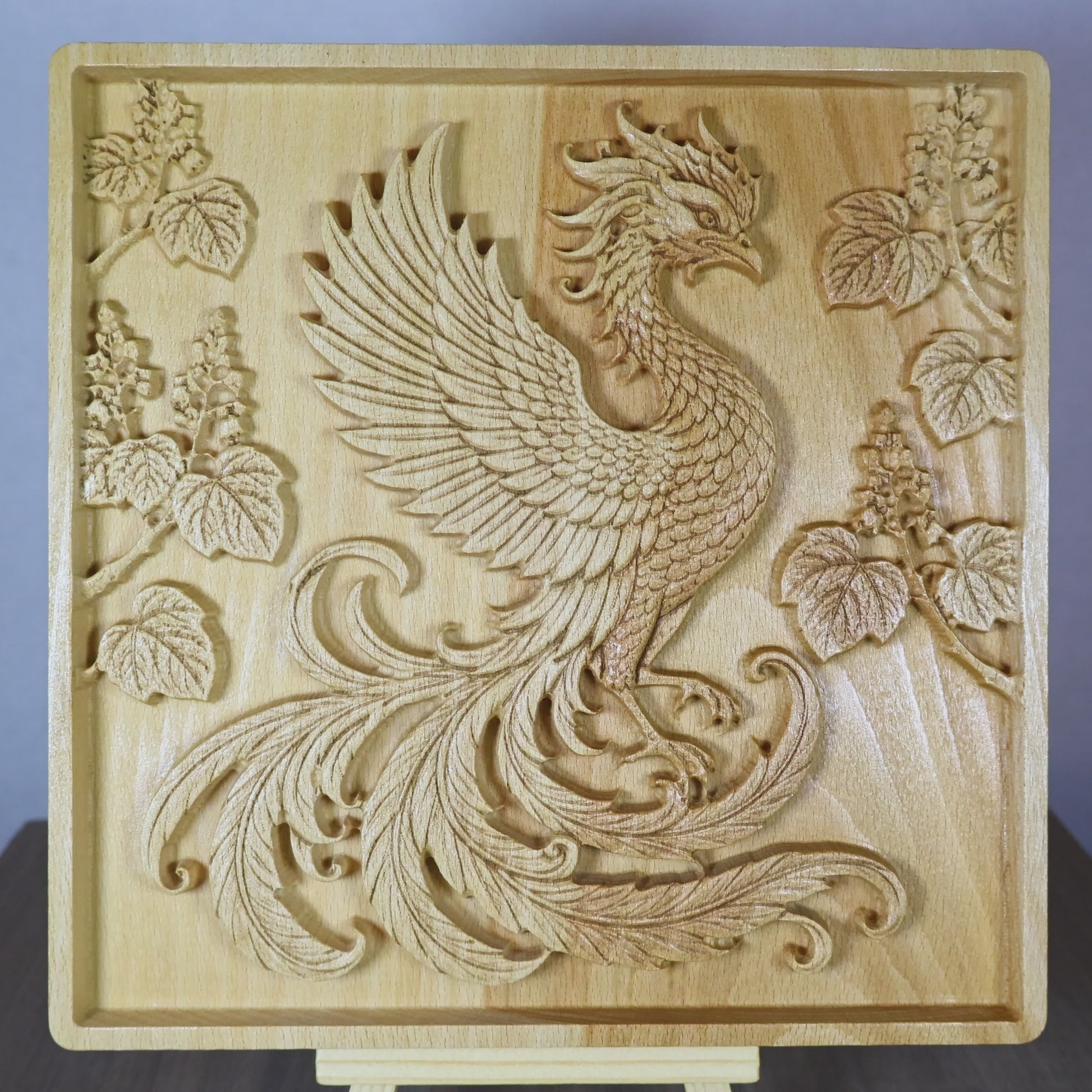 Rotating tabletop video of a Japanese Phoenix wood relief, showing the front and angled side views of the carved Hoo phoenix, flowing tail feathers, paulownia kiri branches, raised relief depth, and natural beech wood finish.