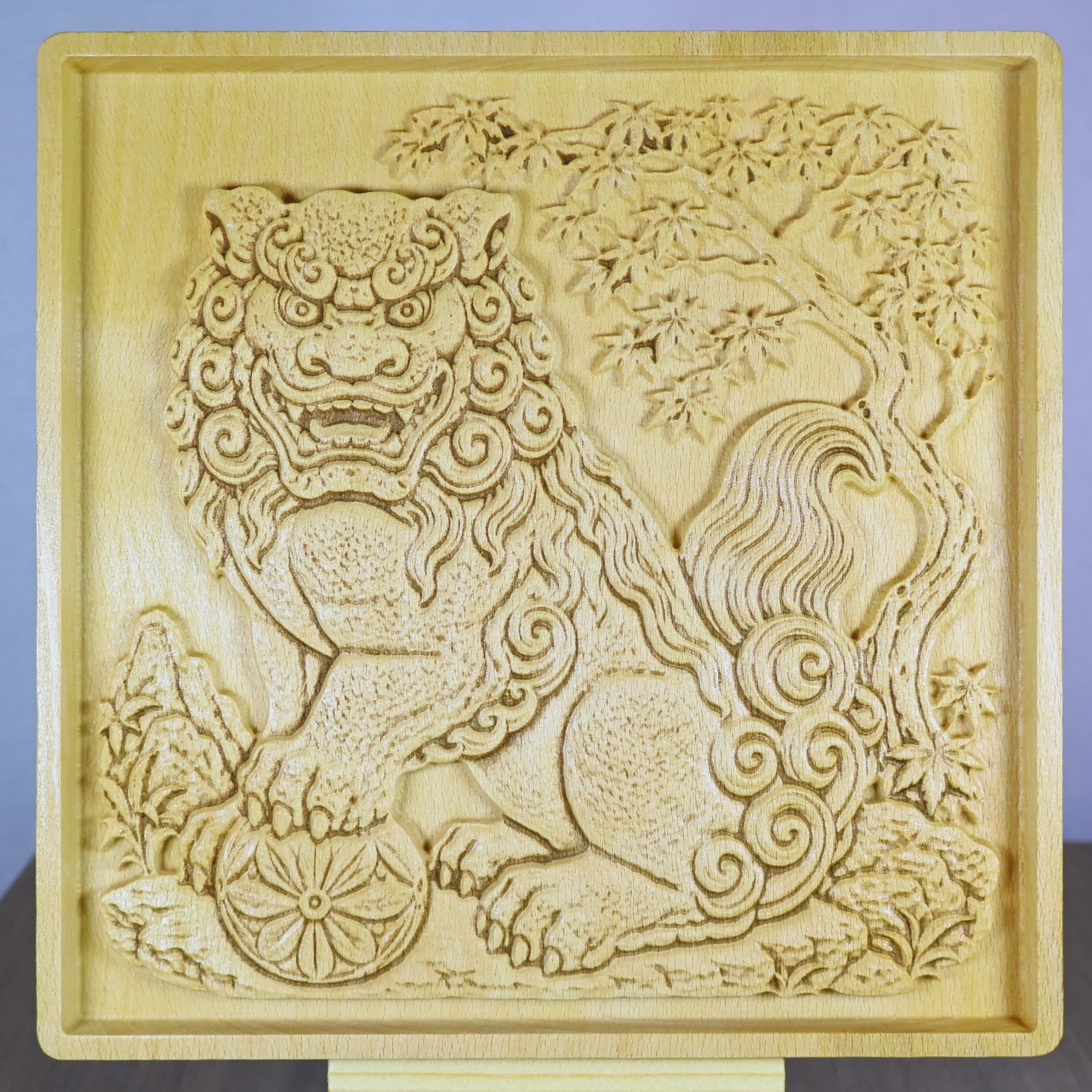 Rotating tabletop video of a Japanese Komainu guardian lion dog wood relief, showing the front view and angled side views with carved temple guardian details, paw on floral ball, curled mane, tree background, raised bas relief depth, and natural wood finish.