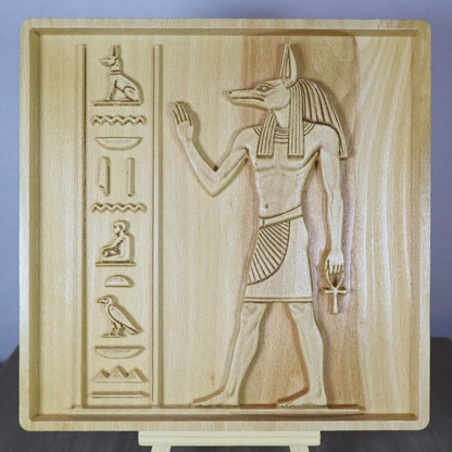 Rotating tabletop video of an Anubis wood relief, showing the front and angled side views of the Egyptian jackal-headed god, raised hand, ankh, hieroglyphic-style carvings, relief depth, and natural beech wood finish.